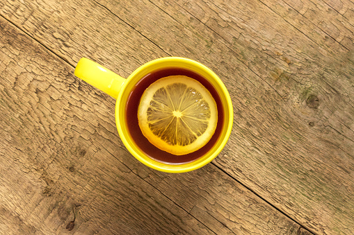 Tea with lemon in a yellow mug on a wooden background .Top view.Copy space for text