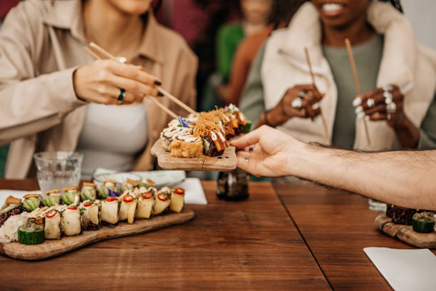 地元のレストランでビーガン寿司を共有することを楽しんでいる友人 - 日本食 ストックフォトと画像