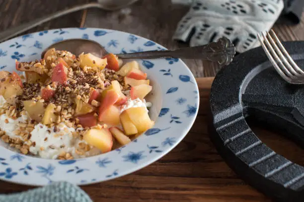 Homemade healthy body building breakfast for muscle gain with cottage cheese, roasted hazelnuts, linseeds and sauteed apples. Served on a deep plate with spoon on wooden table with dumbbell