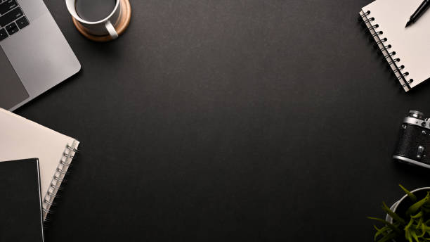 istock Modern black dark workspace background with copy space surrounded by office equipments. 1401695313