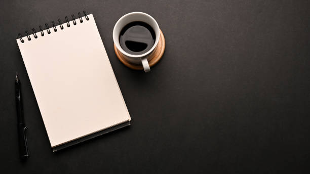 istock Black workspace table with a cup of coffee, an empty spiral notepad and copy space 1401695895