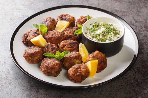 Keftedakia is a Greek traditional dish that is created with minced beef and bread crumbs rolled into balls and fried closeup on a white plate on a table. Horizontal