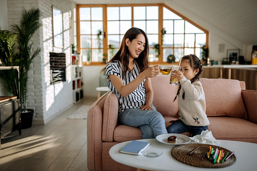 Cute little girl having small celebratory toast with her mother in their living room