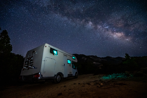 Motorhome RV parked under stars on a pier by the sea, Crete, Greece. Travelers with camper van are resting overnight under milky way on an active family vacation, Crete, Greece.