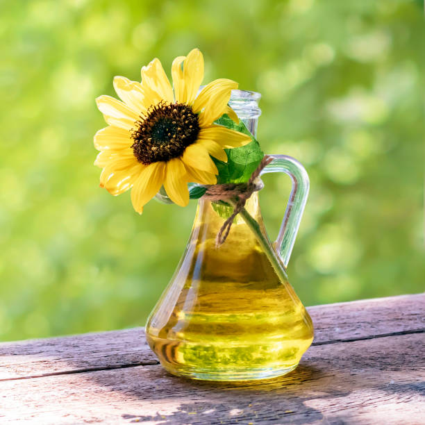 flasche sonnenblumenöl und sonnenblumenblüten mit samen auf einem grünen, verschwommenen hintergrund. - sunflower seed oil stock-fotos und bilder
