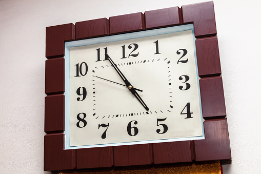 Wall vintage wooden clock with a pendulum on a brick wall. Mechanical watch with Roman numerals on the dial. Light background.