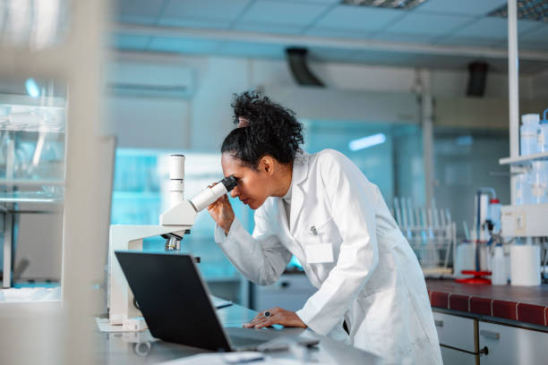 femme scientifique regardant au microscope et utilisant un ordinateur portable dans un laboratoire - microscope laboratory scientist women photos et images de collection