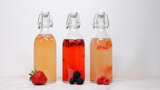 3 kombucha tea swing top bottles on a table, flavored with strawberry, blackberry and raspberry with copy space