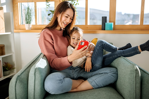 Mother and cute little daughter using phone together to watch cartoons