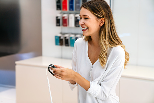 Portrait of happy smiling woman shopping a new smart watch in tech store. Technology people gadget device concept