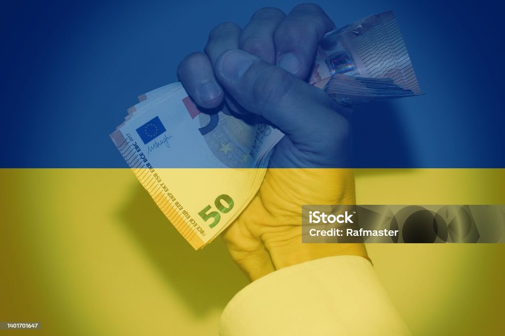 Hand holding european banknotes with the Ukrainian flag as background. Concept of Financial help from Europe. Abundance Stock Photo