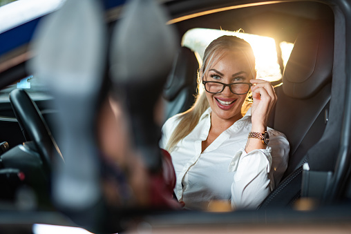 Smiling businesswoman wearing eyeglasses and looking at camera while sitting in car