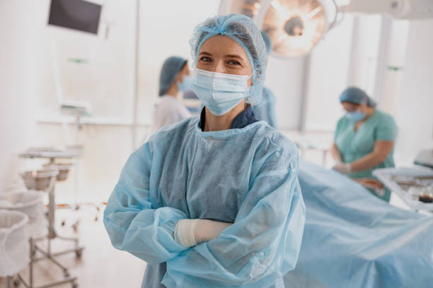 Female surgeon in mask standing in operating room with crossing hands, ready to work on patient stock photo