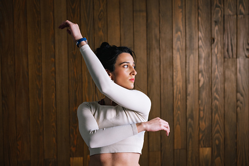 A slim muscular Caucasian sportswoman moving her arms in front of a wooden wall while doing her training.