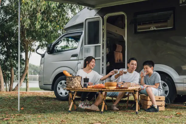 Photo of Happy Asian family talking at picnic table by the camper trailer in nature