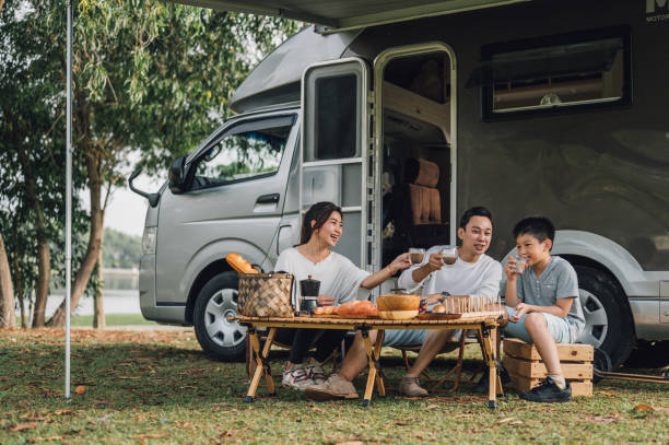 szczęśliwa azjatycka rodzina rozmawiająca przy stole piknikowym przy przyczepie kempingowej w przyrodzie - travel trailer zdjęcia i obrazy z banku zdjęć