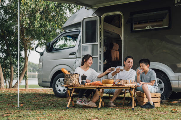 happy asian family talking at picnic table by the camper trailer in nature - acampando imagens e fotografias de stock