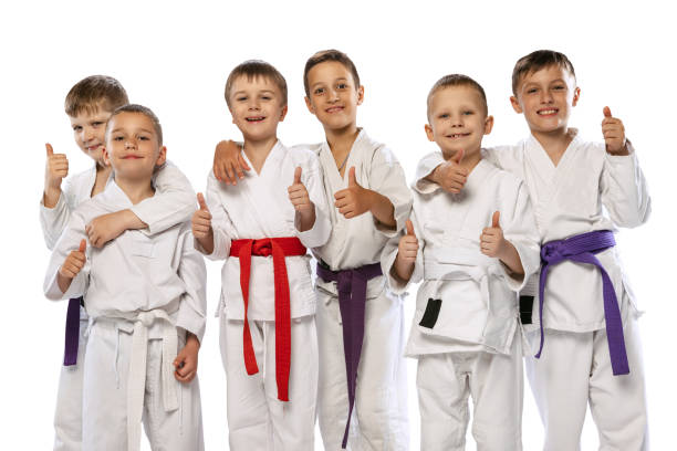 gruppo di bambini felici, combattenti di karate principianti in dobok bianchi in piedi insieme isolati su sfondo bianco. concetto di sport, arti marziali, educazione - extreme sports karate sport exercising foto e immagini stock
