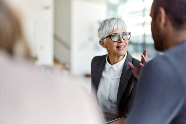 female insurance agent talking to her customers on a meeting in the office. - finance senior adult financial advisor meeting imagens e fotografias de stock