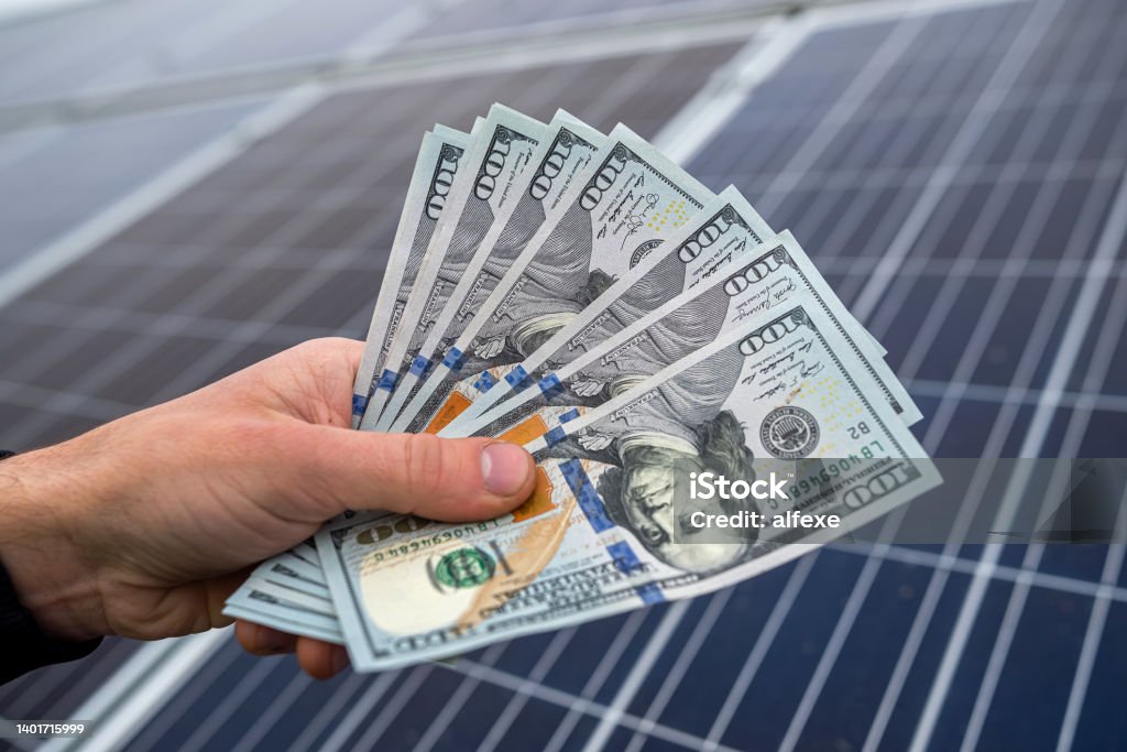 beautiful young gorgeous worker hands holding round sum of money for installing solar panels. beautiful young gorgeous worker hands holding round sum of money for installing solar panels. Green electricity and dollars concept Currency Stock Photo