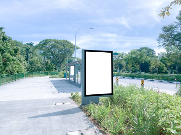 istock Vertical blank advertising poster banner mockup at empty bus stop shelter by main road, greenery behind; out-of-home OOH vertical billboard media display space. 1401716543