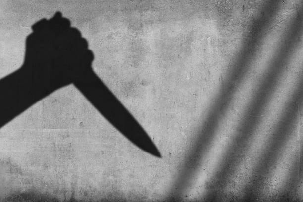 Shadow of the hand holding a knife on wall background stock photo