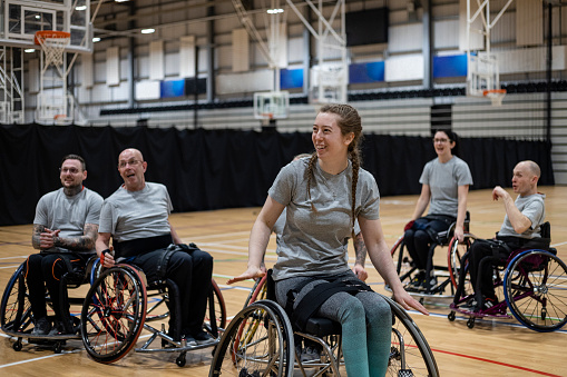 Wide shot of a team of wheelchair users playing basketball in the North East of England. They are competing against one another, laughing and having fun.