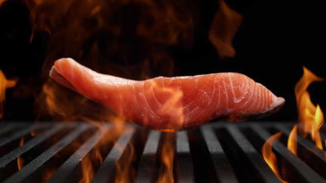 Salmon Fillet Falling onto the Grill Grate Flaming in Slow Motion - BBQ on Black Background