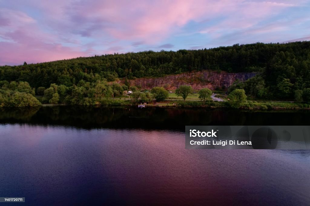 Carrickreagh abandoned Quarry from Lough Erne with rose sunset water reflections. Drone aerial view of Carrickreagh abandoned Quarry from lake Erne with rose sunset water reflections, green forest and lookout point. Lough Erne, Northern Ireland. Color Image Stock Photo
