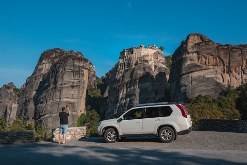 Greece car travel concept. Man standing near suv looking at meteora monastery thessaly mountains