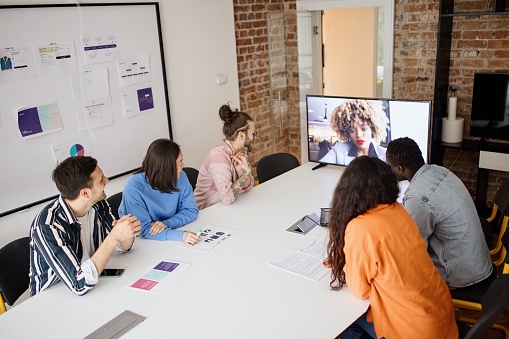 Business people sitting in a meeting room with virtual attendee on the screen
Multiracial group of people on a video conference meeting in hybrid office space.