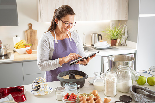 Woman in kitchen using digital tablet while bake a cake. High resolution 42Mp indoors digital capture taken with SONY A7rII and Zeiss Batis 40mm F2.0 CF lens