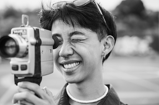 Young asian man using vintage old video camera outdoor - Focus on right eye - Black and white editing