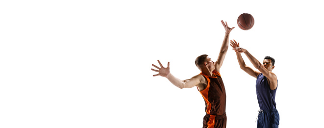 Portrait of two young men, professional basketball players in motion, training isolated over white studio background. Scoring a goal. Concept of sport, team game, action, active lifestyle, ad