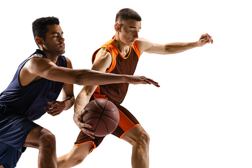 Portrait of two young men, professional basketball players in motion, playing, dribbling isolated over white background. High concentration. Concept of sport, team game, action, active lifestyle, ad