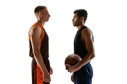 Portrait of two young men, basketball players looking at each other, posing isolated over white studio background. Game opponent. Concept of sport, team game, action, active lifestyle, ad