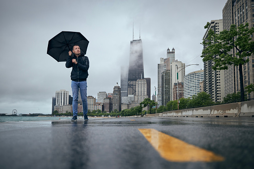 Rainy and windy day in city. Man with umbrella walking against Chicago cityscape.