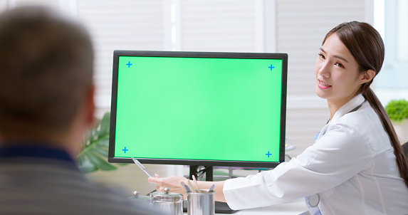 attractive young brunette ponytail female asian doctor wear white coat and stethoscope show green screen computer to gray hair old sick man in clinic - she pen pointing explaining