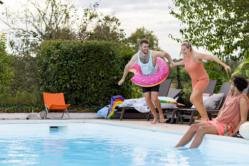 A full length side view of two friends holding hands as they jump into the swimming pool of the villa they are staying at in Toulouse in the South of France.