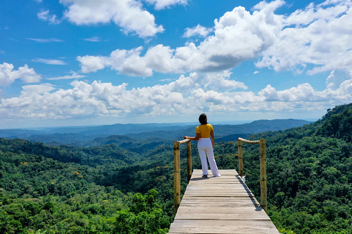 A tourist in south america of hispanic ethnicity is walking over a viewpoint that shows a vast tropical forest, relaxing nature background