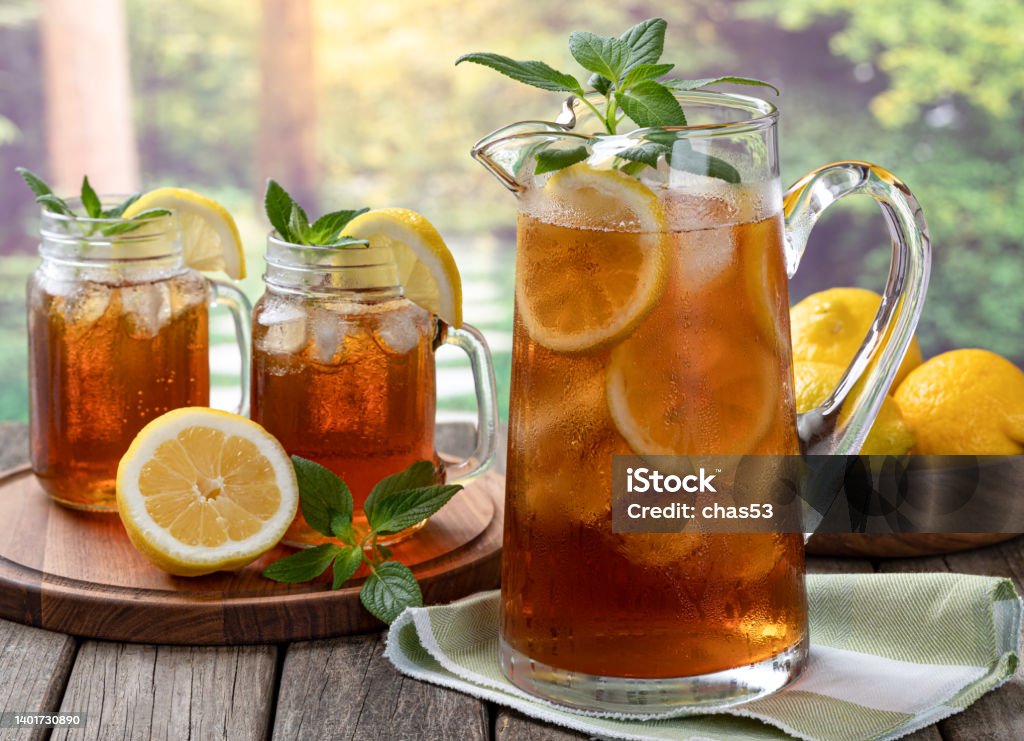 Pitcher of cold ice tea with rural summer background Pitcher of cold iced tea with mint, lemon slices and ice with two glasses ot tea on a wooden table and rural summer background Ice Tea Stock Photo