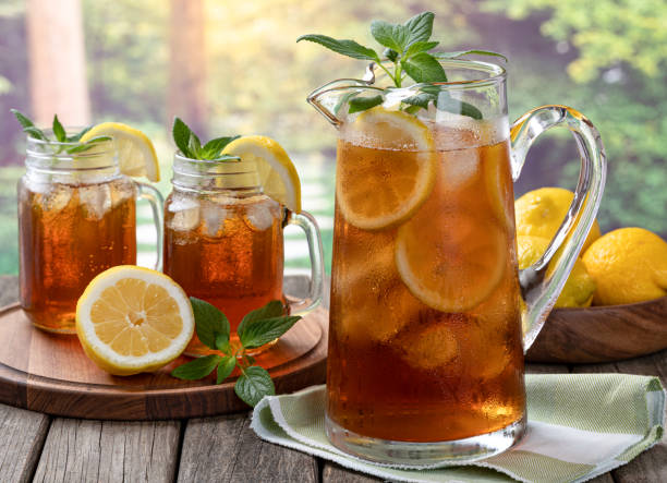 Pitcher of cold ice tea with rural summer background Pitcher of cold iced tea with mint, lemon slices and ice with two glasses ot tea on a wooden table and rural summer background tea stock pictures, royalty-free photos & images