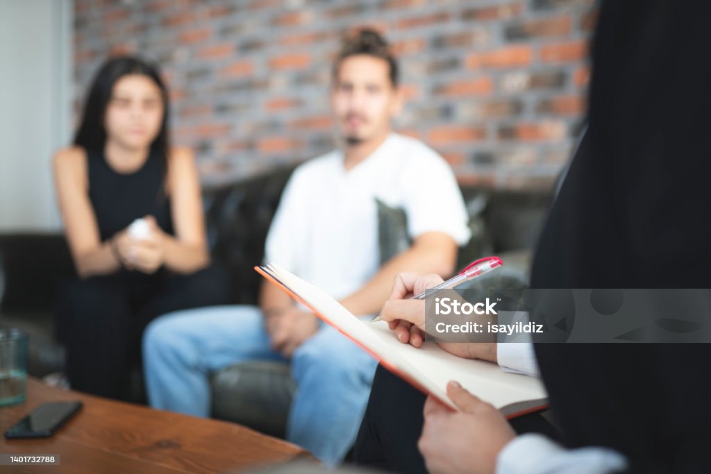 Psychologist is listening to problems of young couple Young couple having session with psychologist at office. Psychologist is talking about problems. Young couple is listening to her. Couple - Relationship Stock Photo