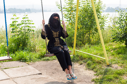 Muslim woman riding on a swing national black Islamic clothing.