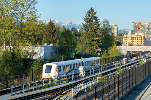 Port Moody, BC, Canada - April 20 2021 : Millennium Line SkyTrain. Moody Centre station. City skyline and nature landscape in the background. Urban transportation concept.