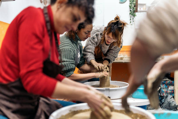 Pottery Group_Ana Barriuso.jpg, Pottery Group_Patricia Delgado.jpg, Pottery Group_Elena Vazquez.jpg, Pottery Group_Gabriela Levinton.jpg, Pottery Group_Property.jpg, Pottery Group_Espacio.jpg Stock photo of pottery teacher explaining to concentrated woman how to use spinning wheel. homemade pottery wheel stock pictures, royalty-free photos & images