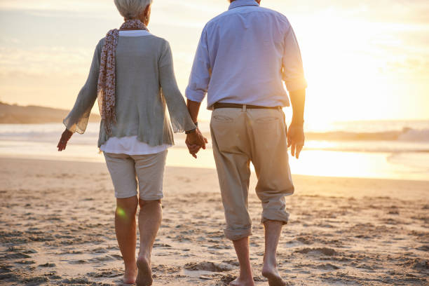 istock Senior couple holding hands while walking along a sandy beach at sunset 1401738858