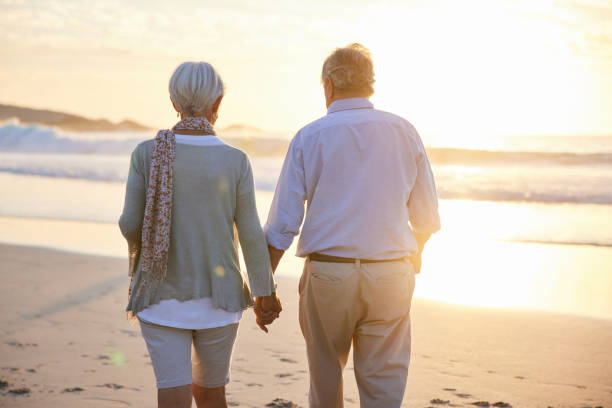 istock Senior couple holding hands and walking on a beach at sunset 1401739065
