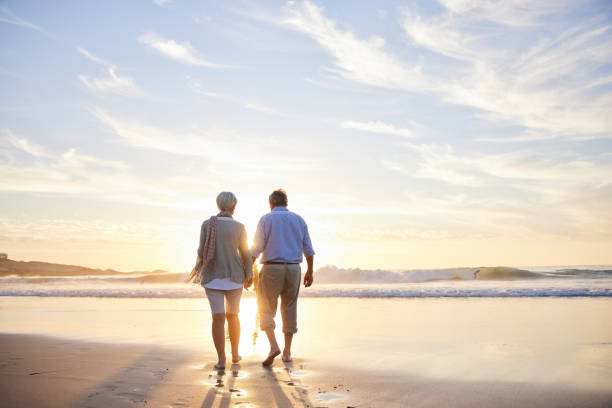 Loving senior couple walking hand in hand on a beach at sunset stock photo