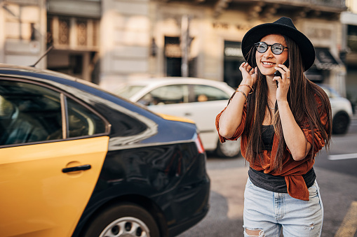 Young fashionable asian woman calling a cab on the street